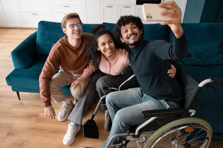 Three individuals in wheelchairs smiling and taking a selfie together, showcasing friendship and inclusivity.
