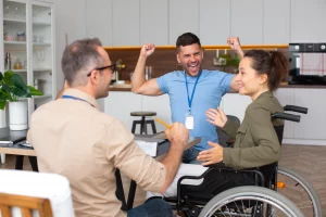 A man in a wheelchair is seated with two women, engaged in conversation around him.