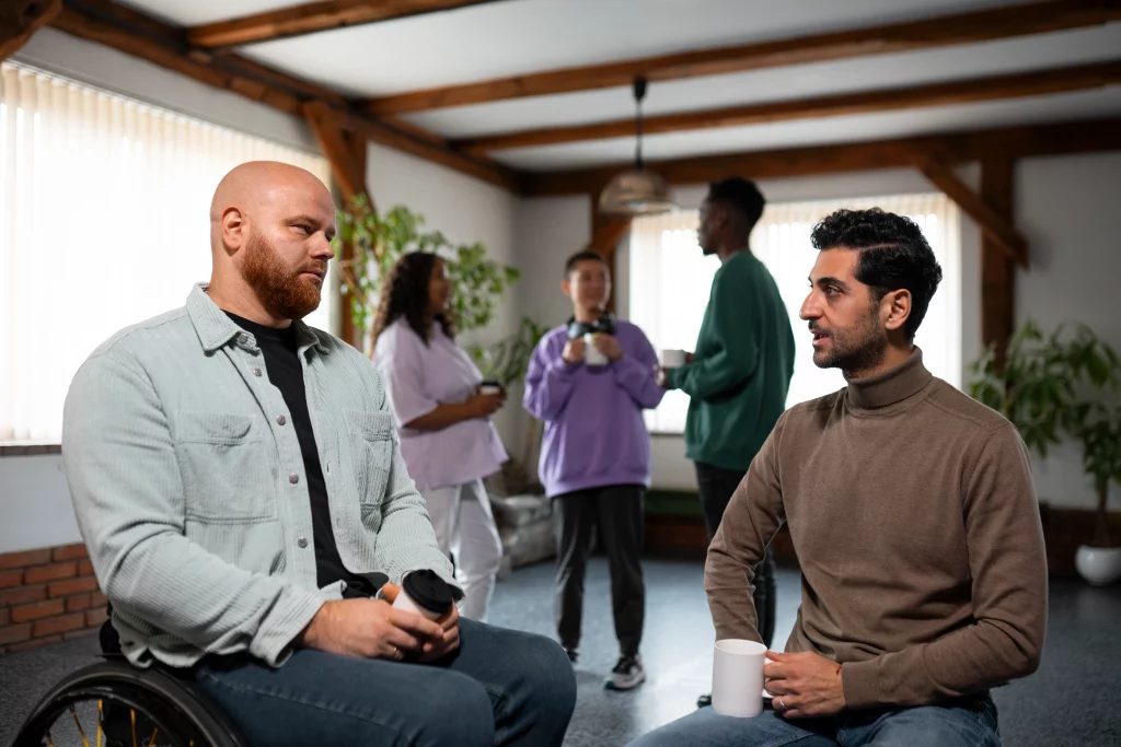 A man in a wheelchair engages in conversation with another man standing beside him.