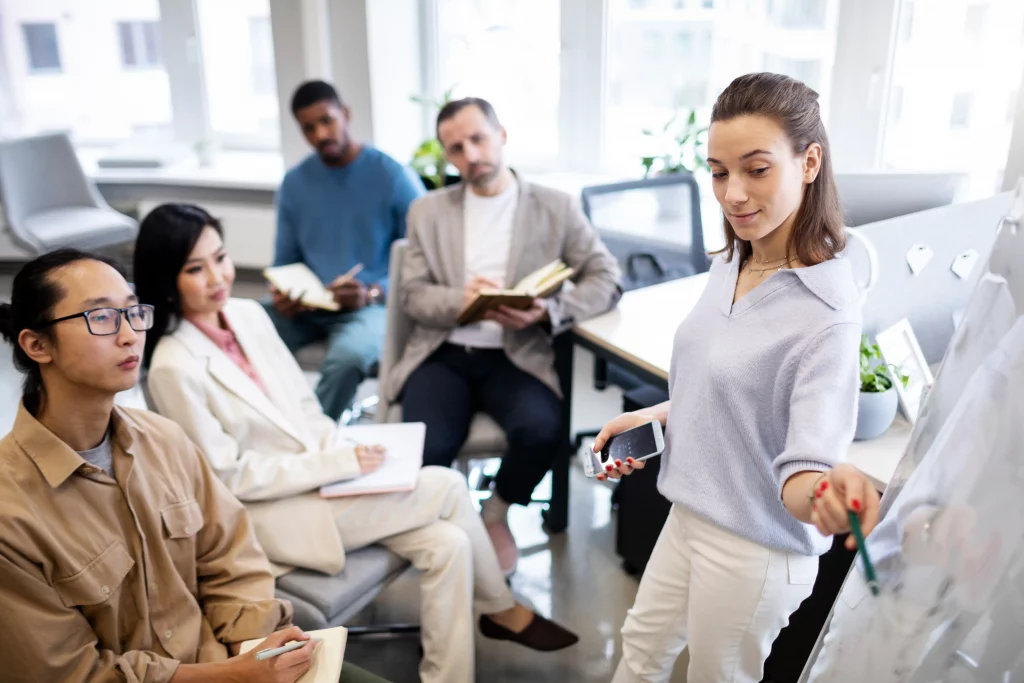 A group of professionals engaged in a meeting, with one person presenting ideas on a whiteboard while others take notes.