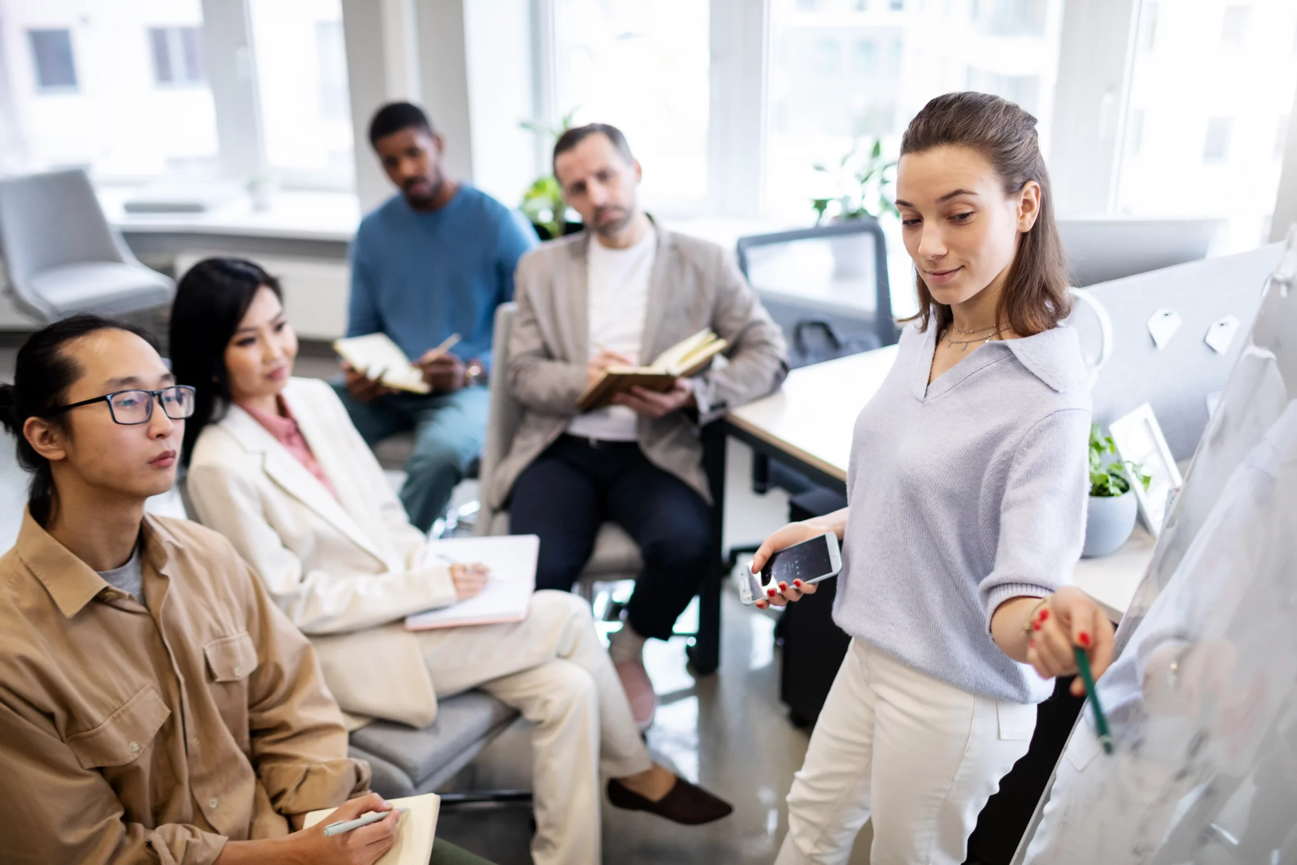 A group of professionals engaged in a meeting, with one person presenting ideas on a whiteboard while others take notes.
